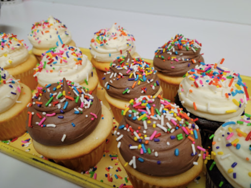 A tray of colorful cupcakes with chocolate and vanilla frosting, topped with vibrant sprinkles.