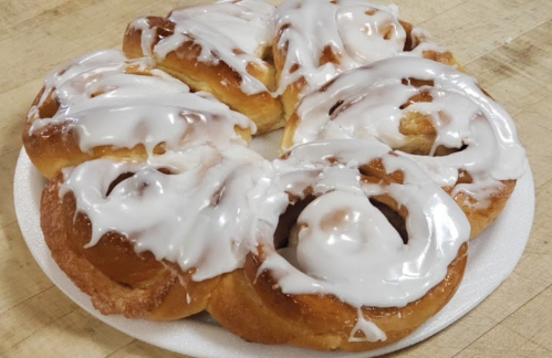 A plate of freshly baked cinnamon rolls topped with white icing, arranged in a circular pattern.