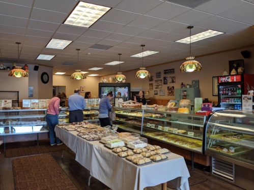 A bakery interior with display cases of pastries, customers browsing, and vintage decor. Warm lighting and a cozy atmosphere.