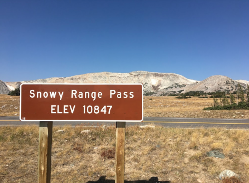 Sign for Snowy Range Pass at an elevation of 10,847 feet, with mountains and clear blue sky in the background.