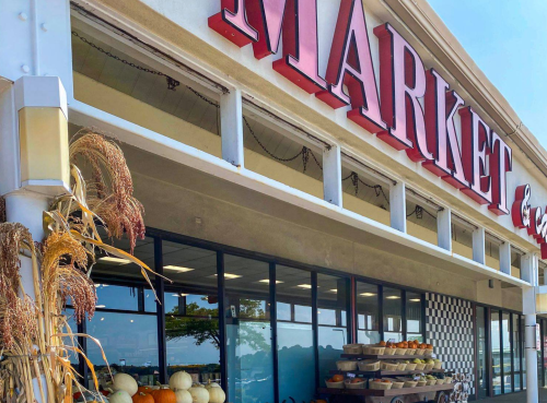 Exterior of a market with a large sign, featuring pumpkins and decorative plants in front. Bright and inviting atmosphere.