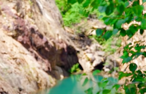 A blurred natural landscape featuring rocky formations and a turquoise body of water surrounded by greenery.