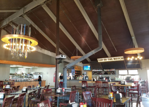 Interior of a restaurant with high ceilings, wooden tables, and a bar area, featuring modern lighting and a welcoming atmosphere.