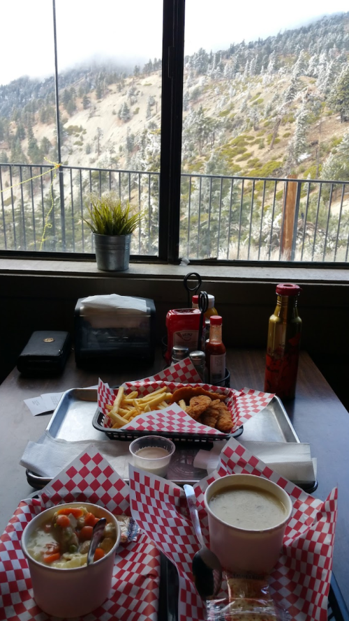 A table with two trays of food, including soup and fries, with a scenic mountain view through a window.