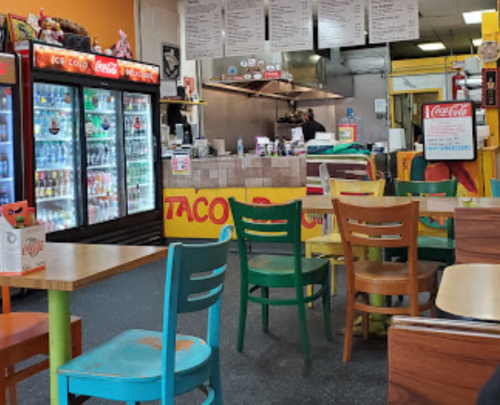 Colorful chairs and tables in a casual eatery with a taco counter and drink coolers in the background.