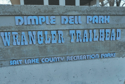 Sign for Dimple Dell Park Wrangler Trailhead, featuring blue lettering on a stone background.