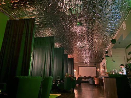 A stylish lounge with a metallic ceiling, dim lighting, and elegant decor, featuring dark curtains and a bar area.