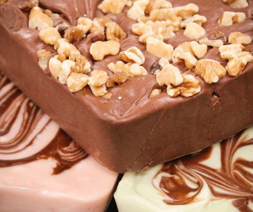Close-up of chocolate fudge topped with chopped walnuts, surrounded by pink and green swirled fudge squares.