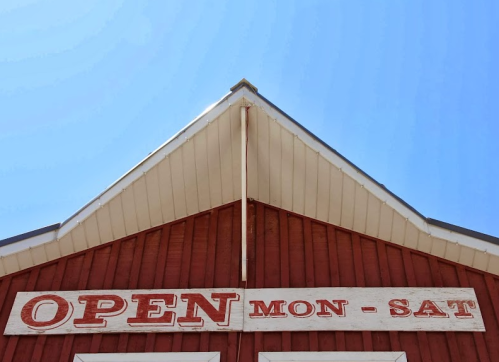 Red barn with a sign reading "OPEN MON-SAT" against a clear blue sky.