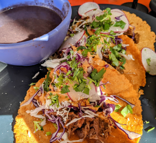Three tacos topped with shredded cabbage, radishes, and cilantro, served with a side of black beans.