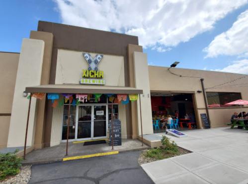 Exterior of Xicha Brewing with colorful decorations, outdoor seating, and a clear blue sky.
