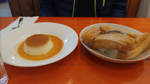 A plate with flan and a bowl of churros on a wooden table, with a glass of water nearby.