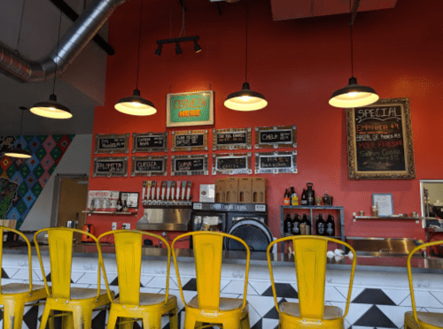 Colorful restaurant interior featuring a red wall, menu boards, and yellow bar stools at a counter.