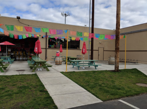 Outdoor seating area with colorful papel picado banners, picnic tables, and umbrellas in a casual setting.