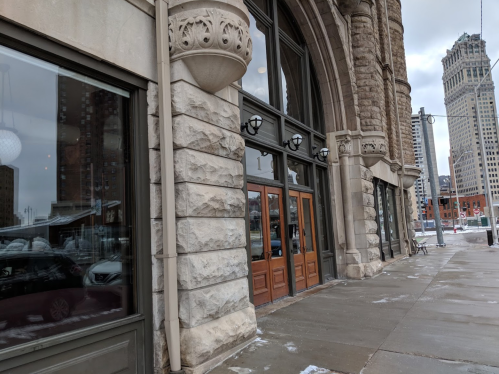 Exterior view of a historic building with large windows and wooden doors, set against a city skyline.