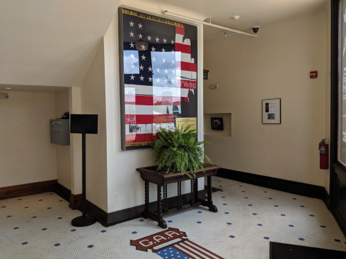 A corner of a room featuring a large American flag artwork, a table, and a potted plant on tiled flooring.