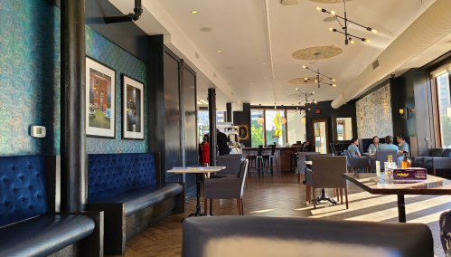 Interior of a modern restaurant featuring blue upholstered seating, artwork on the walls, and patrons dining.