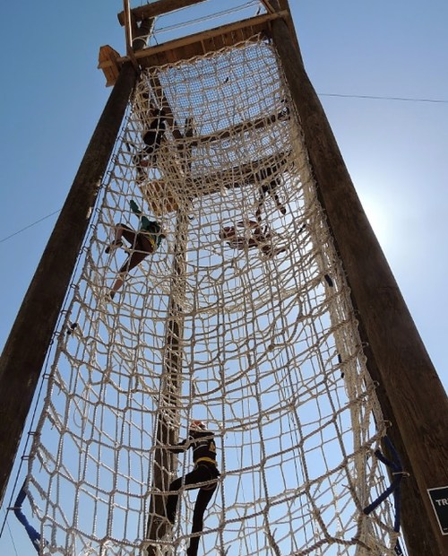 A group of people climbing a large rope net structure against a clear blue sky.