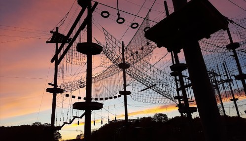 Silhouette of an adventure park with climbing structures against a colorful sunset sky.