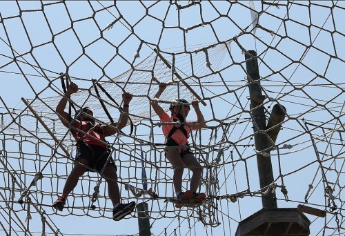 Two children navigate a rope climbing structure against a clear blue sky.