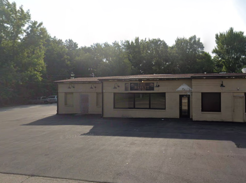 A vacant building with a sign reading "Basket," surrounded by trees and an empty parking lot.