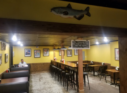 Interior of a casual restaurant with yellow walls, wooden tables, and a lone diner sitting at a booth.