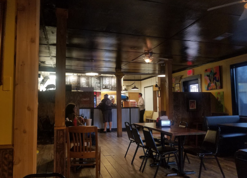 Interior of a casual restaurant with wooden floors, tables, and a counter where customers are ordering food.