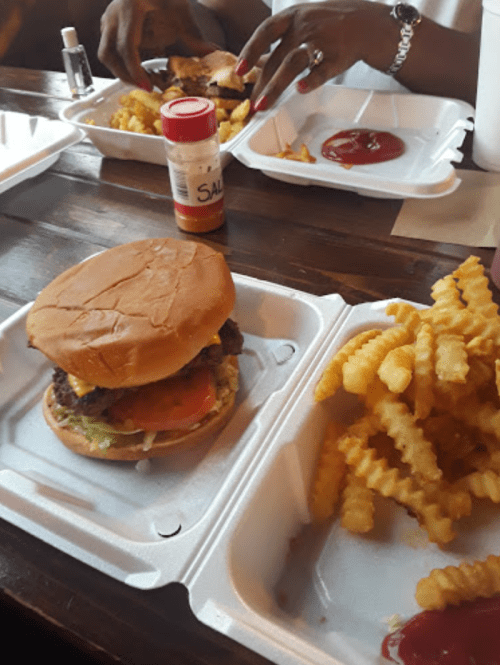 A close-up of a burger with lettuce and tomato, served with crinkle-cut fries and condiments on a table.