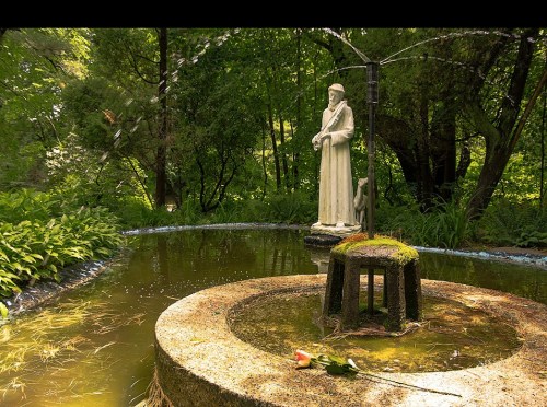 A serene garden scene featuring a statue surrounded by a circular pond and lush greenery.
