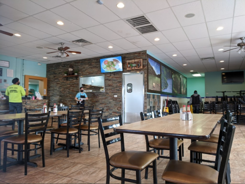 Interior of a restaurant with empty tables, a stone wall, and staff preparing food in the background.