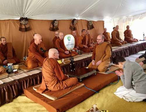 Buddhist monks seated in a tent, engaged in a ceremony, with one monk playing a traditional instrument.