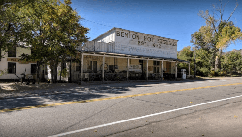 Historic building of Benton Hot Springs, established in 1852, with trees and a clear blue sky in the background.