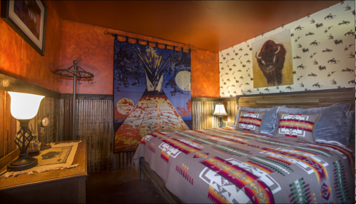 Cozy bedroom with a colorful patterned bedspread, warm orange walls, and Native American-inspired decor.