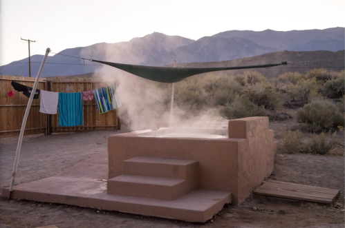 A desert scene at dusk with a steaming hot spring, a clothesline with laundry, and mountains in the background.