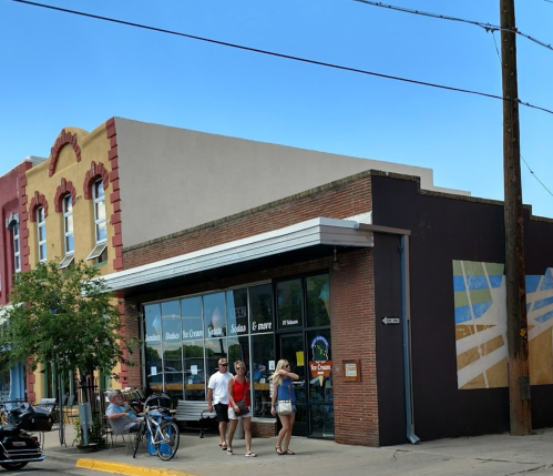 A colorful storefront with people walking by, featuring outdoor seating and a bicycle parked nearby.