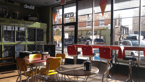 Bright ice cream shop interior with colorful seating, large windows, and a view of the street outside.