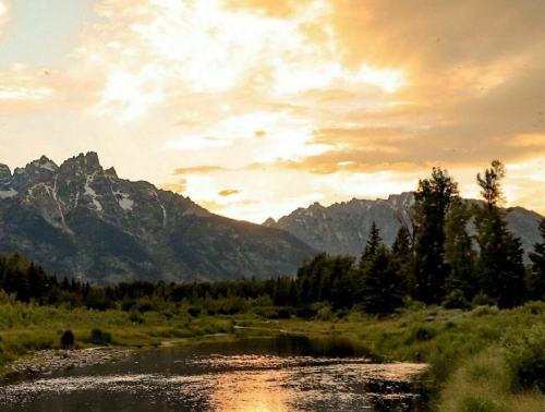 A serene landscape featuring a river, lush greenery, and mountains under a golden sunset sky.