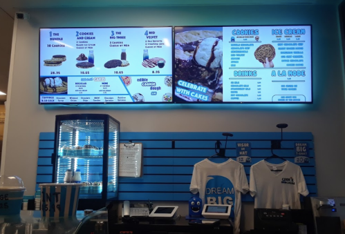 Menu display at a dessert shop featuring cookies, ice cream, cakes, and drinks, with promotional signage.
