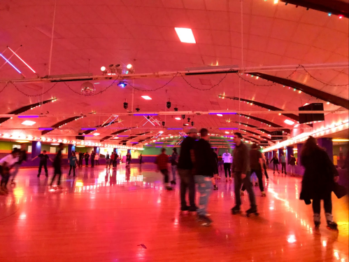 A vibrant roller skating rink filled with people, illuminated by colorful lights and a lively atmosphere.