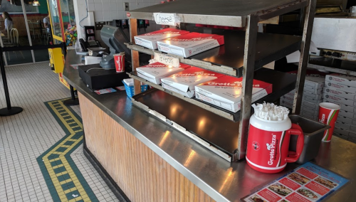 A counter with stacked pizza boxes, drinks, and a condiment holder in a casual dining setting.