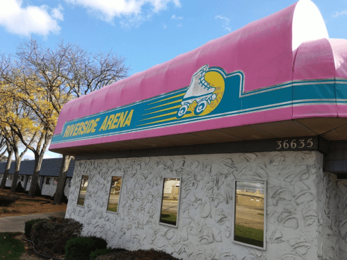 Exterior of Riverside Arena, featuring a pink roof with roller skate graphics and a sign displaying the arena's name.
