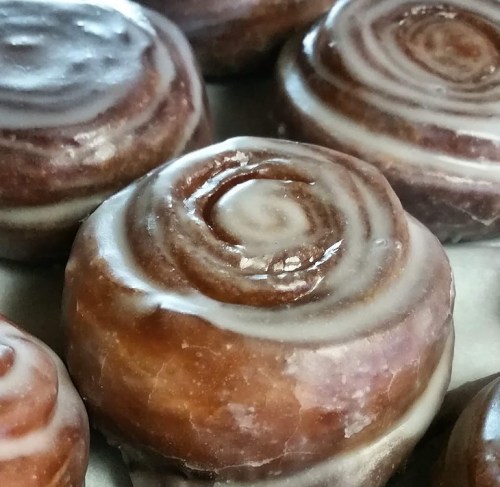 Close-up of glazed cinnamon rolls with a shiny icing swirl on top, arranged in a tray.