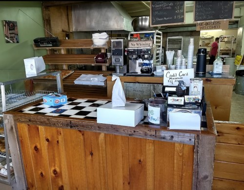A rustic counter at a bakery with coffee machines, baked goods, and a sign for credit card payments.