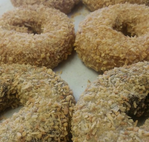 A close-up of several donuts coated in a crunchy, golden-brown topping, arranged on a white surface.