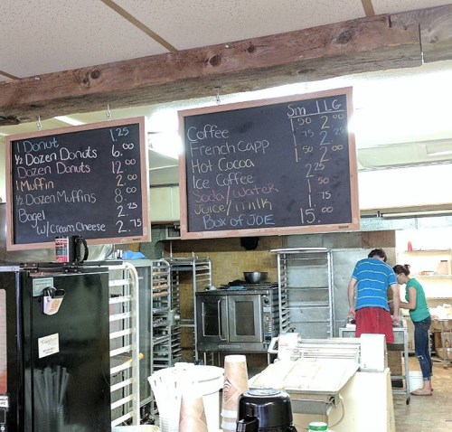 Menu boards displaying prices for baked goods and beverages in a cozy café setting.