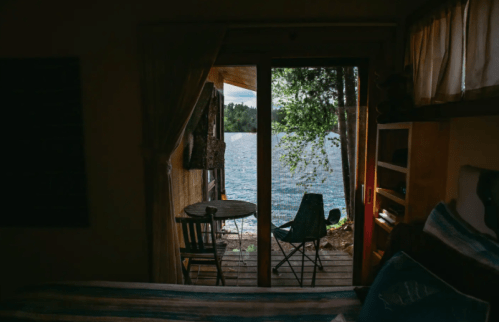 View from a cozy cabin interior, showcasing a lake and trees through a sliding glass door.
