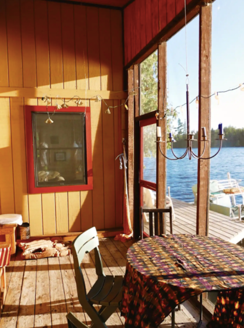 Cozy interior of a lakeside cabin with a table, chairs, and large windows overlooking the water.