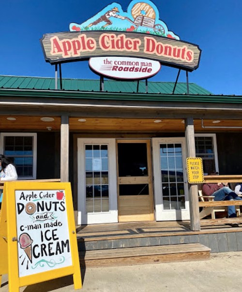 Sign for "Apple Cider Donuts" and "Ice Cream" at a roadside shop with a blue sky in the background.