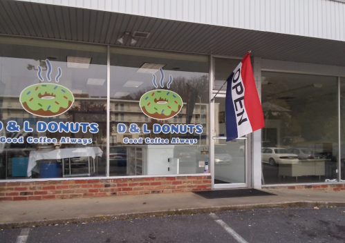Exterior of D & L Donuts shop with a colorful donut logo and an "OPEN" flag displayed outside.
