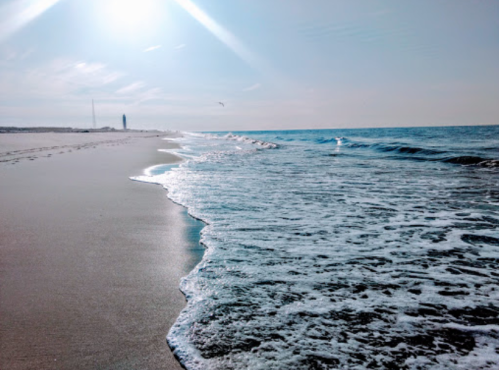 A serene beach scene with gentle waves lapping at the shore under a bright sun.
